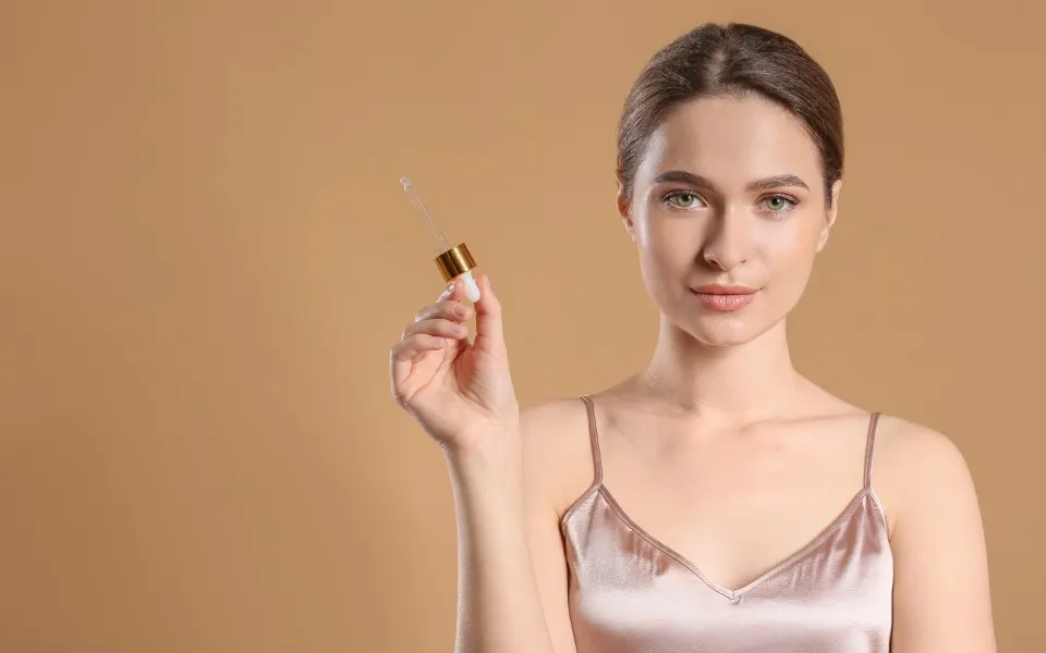 Woman holding a serum dropper against a warm beige background